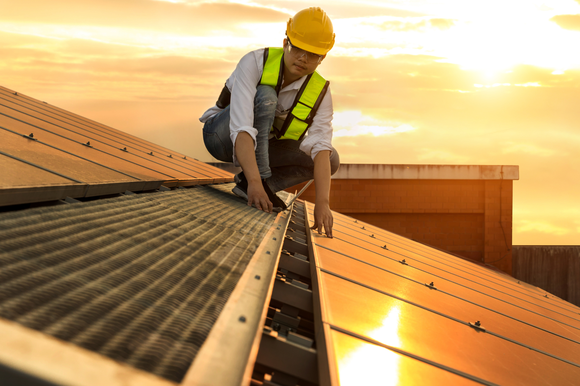 Construction worker laying out solar panels on a roof during sunrise