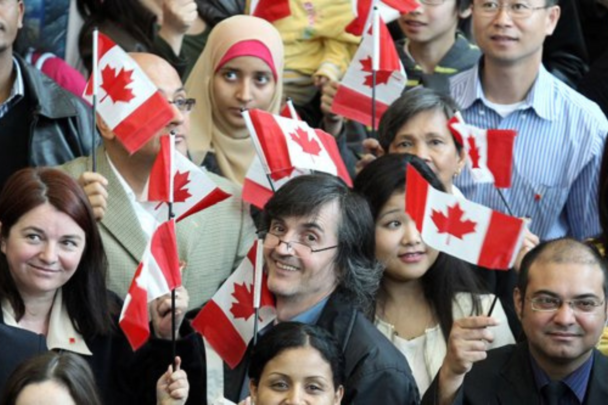 A diverse group of new Canadians waving Canadian flags.