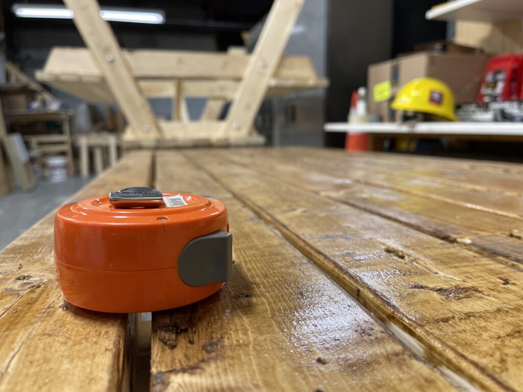 A photo of measuring tape lying on a picnic table in a workshop.