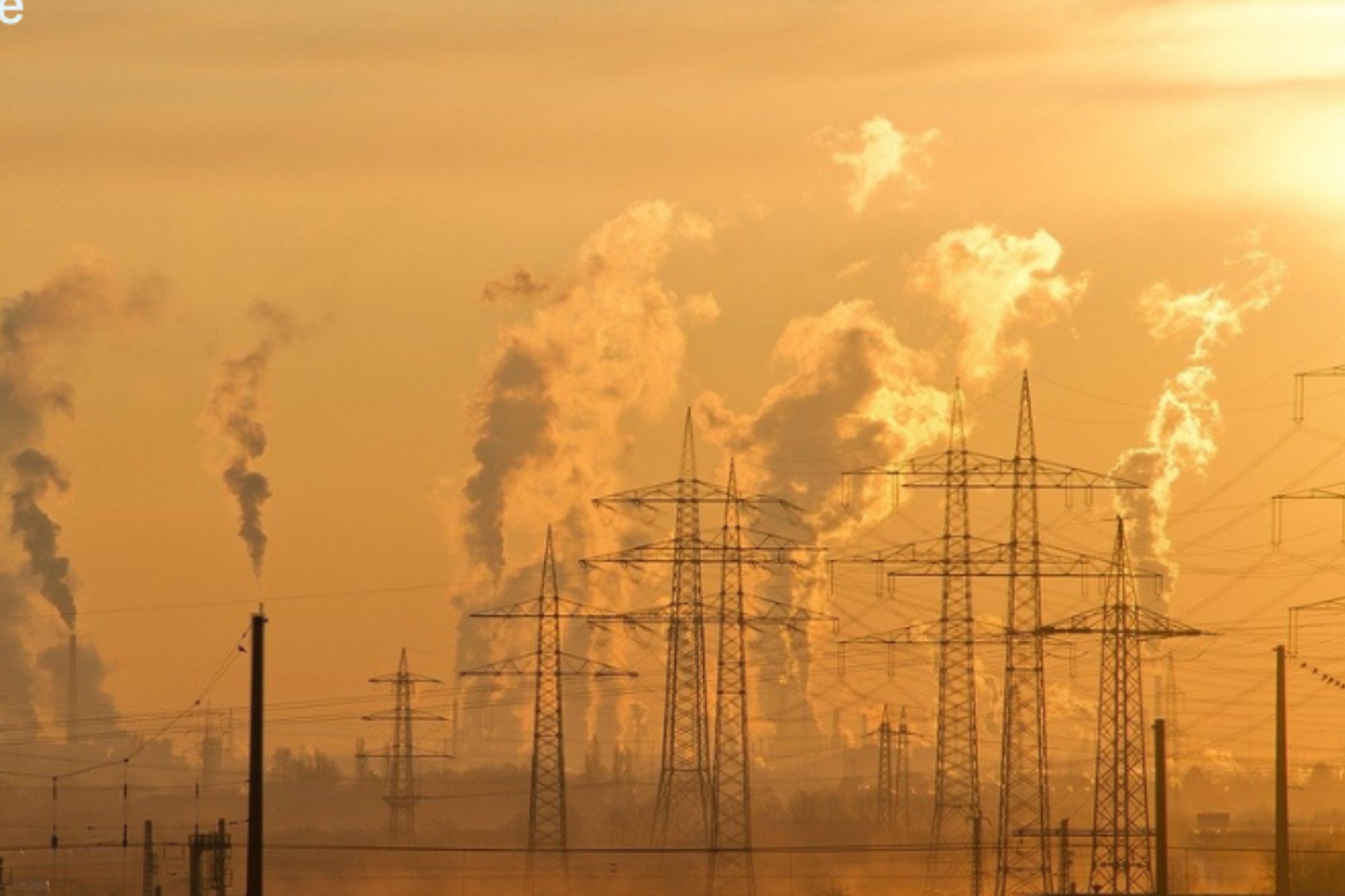 A photo of electrical towers against an orange sky with smoke rising in the background