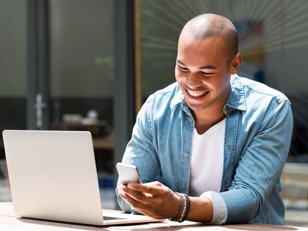 Man looking at a smartphone in front of a laptop