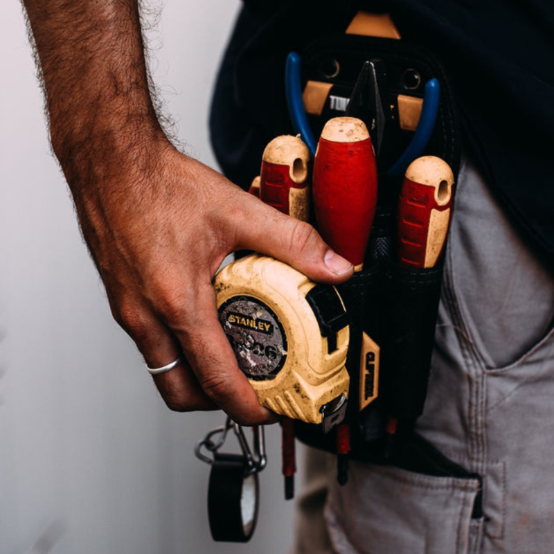 Close-up of a man holding a tape measurer against his toolbelt.