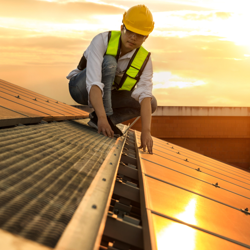 Construction worker laying out solar panels on a roof during sunrise