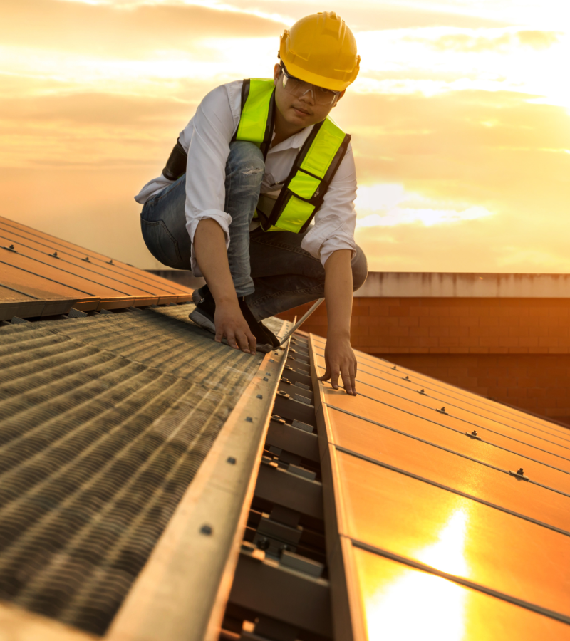 Construction worker laying out solar panels on a roof during sunrise